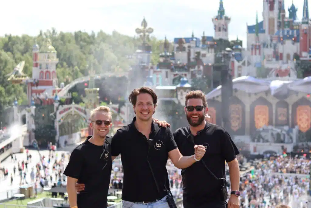 Drie teamleden op Tomorrowland met het hoofdpodium op de achtergrond