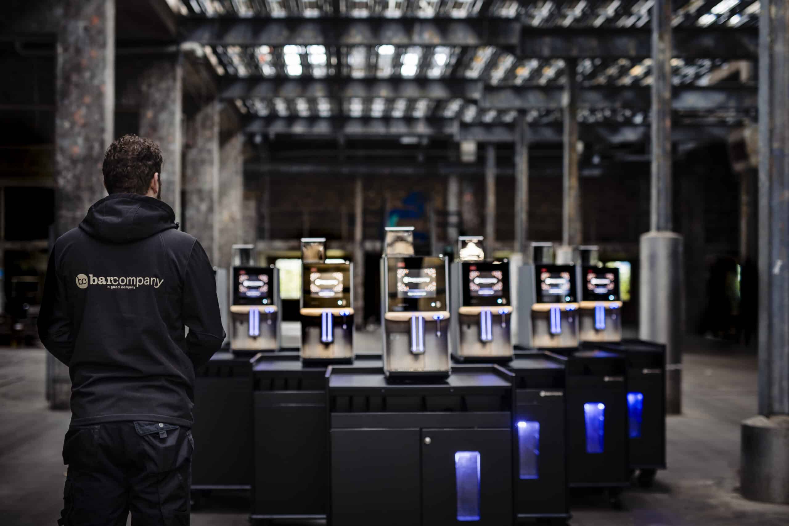 Collega van Bar Company Koffiemachines in de loods, bij een rij koffiemachines