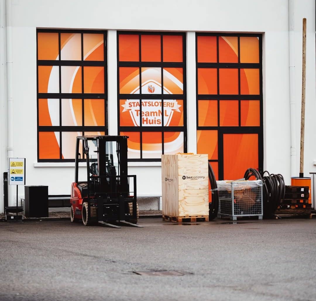 Houten kist van Bar Company en materiaal klaar voor levering bij de gevel van het Staatsloterij TeamNL Huis in Milaan